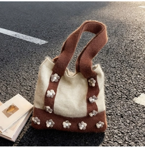 Outdoor close-up of a knit floral tote bag with crochet flower details on asphalt