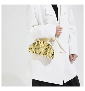 Detail of gold wrinkled texture acrylic clutch bag with metallic chain on white suit