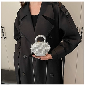Detail of silver rhinestone evening box bag with metal handle worn on a black trench coat