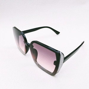 Detail of oversized black frame sunglasses with purple gradient lenses and silver glitter