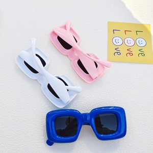 Flat lay of retro thick frame sunglasses in blue, white, and pink with dark lenses