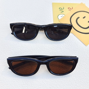 Classic black oval sunglasses with dark gray and brown lenses on a white textured surface