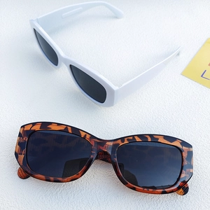Detail view of white and tortoiseshell cat eye sunglasses with dark lenses on textured surface