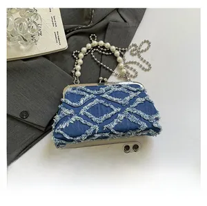 Detail of blue denim shell bag with beaded handle and metal clasp next to a phone