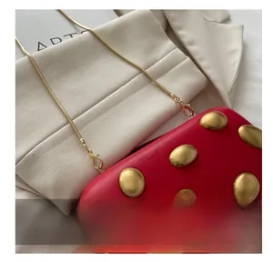 Détail de sac de soirée en cuir rouge avec clous dorés et bandoulière en chaîne métal