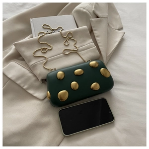 Pochette en cuir vert foncé avec accents dorés et chaîne à côté d'un smartphone