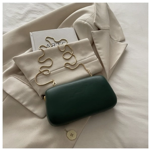 Détail d'une pochette vert foncé avec chaîne serpent dorée sur un blazer beige chic
