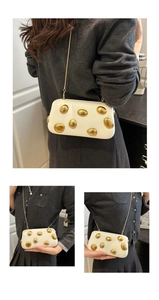 Détail du sac boîte en cuir blanc avec accents dorés et bandoulière chaîne élégante