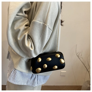 Détail de pochette en cuir noir avec clous dorés irréguliers et bandoulière chaîne