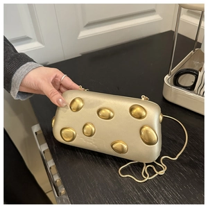Détail de la pochette de soirée dorée à coque rigide avec rivets métalliques et chaîne