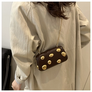 Détail du mini sac boîte marron chocolat avec rivets dorés et chaîne sur trench beige