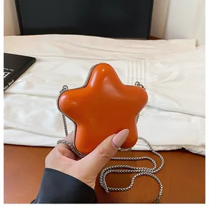 Close-up of a star-shaped orange mini bag with a silver chain held in hand