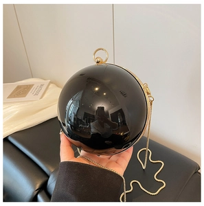 Dettaglio di una borsa da sera sferica nera lucida con manico in metallo dorato e catena