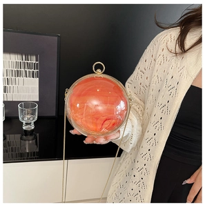 Detail of creative orange marble sphere bag with gold circular handle and chain