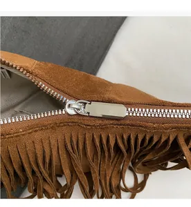 Detail of smooth metal zipper and bohemian suede fringe on the brown crossbody bag