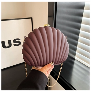 Detail shot of a dark purple shell-shaped handbag with a gold metal clasp and chain strap