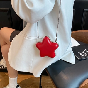 Star-shaped mini red patent leather crossbody bag with silver chain on white suit