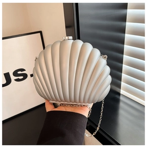 Detail of a pearlescent shell-shaped clutch bag with silver metal chain and glossy texture
