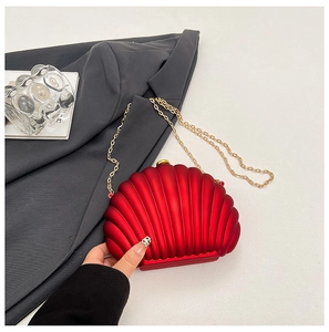 Macro detail of red shell-shaped evening bag with golden chain and matte texture