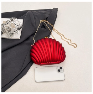 Macro detail of red shell-shaped evening bag with gold chain next to smartphone for scale