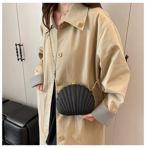 Detail of black shell-shaped evening bag with gold chain and radial texture on beige coat