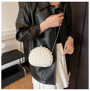 Chic shell-shaped acrylic clutch bag with silver chain strap worn on a black leather jacket