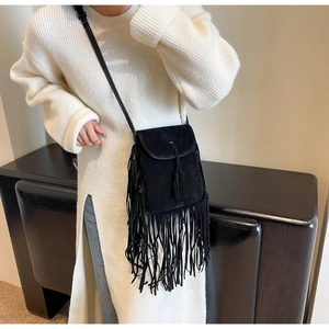 Détail d'un sac à bandoulière noir bohème à franges sur un pull en tricot blanc contrasté