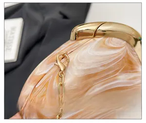 Detailed close-up of golden metal clasp on amber marble acrylic evening clutch bag