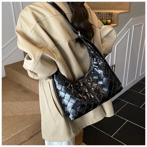 Detailansicht einer schwarzen gewebten Hobo-Tasche an einem Modell im beigen Blazer