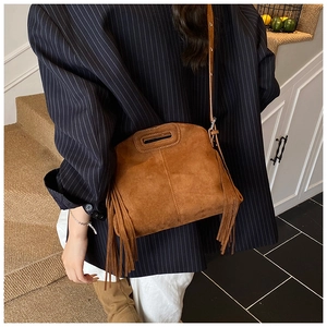 Detail of brown suede crossbody bag with long side tassels and handle, worn with a blazer