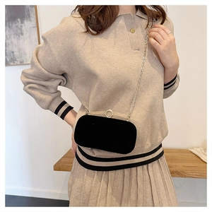 Detail shot of the black velvet evening bag with gold chain worn across a beige outfit