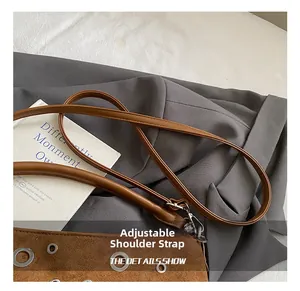 Détail d'une bandoulière en cuir réglable avec œillets métalliques sur un sac marron