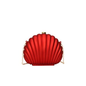 Detailed view of red shell clutch bag with gold cylindrical clasp and chain strap