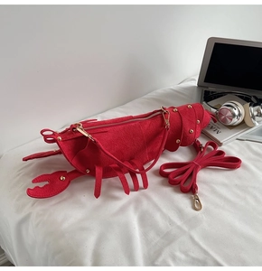 Detail of red lobster-shaped shoulder bag in matte finish with gold zipper on a bed