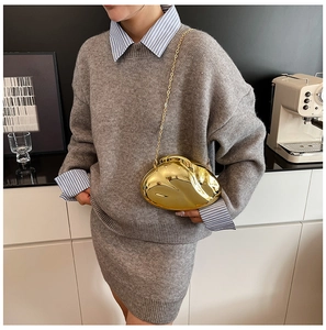 Detail shot of a golden bean-shaped metallic clutch with a thin chain strap on a model