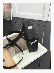 Detalle de bolso caja negro con cierre de metal plateado y gancho para correa