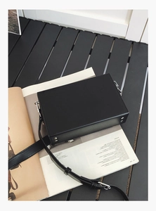 Detalle del bolso bandolera negro tipo caja con remaches plateados y herrajes metálicos