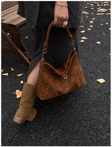 Détail du sac à bandoulière en daim marron avec œillets métalliques sur un banc d'automne