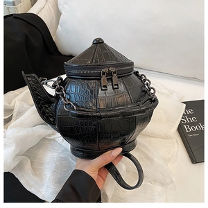 Detail of 3D kettle-shaped handbag in black crocodile texture with metal chain