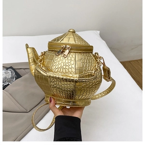 Macro detail of golden teapot-shaped bag with crocodile embossed leather and gold chain