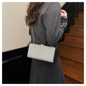 Silver glitter clutch bag with metallic chain shown on shoulder in stylish indoor setting