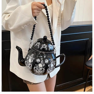Close-up of gothic teapot bag with white skull motifs and beaded handle on a white blazer