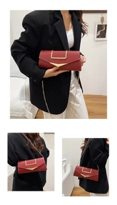 Detail of red leather envelope bag with gold geometric clasp and fine metal chain