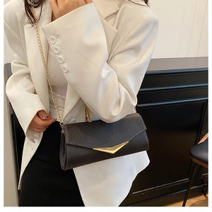 Detail of black pebbled leather crossbody bag with V-shaped gold clasp and chain strap