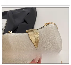 Detail of elegant champagne evening clutch with leaf clasp and gold chain strap