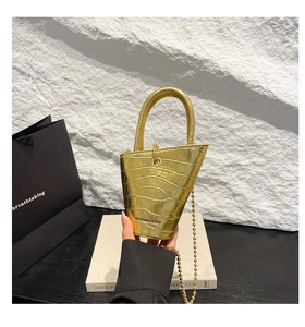 Detail of gold crocodile pattern mini bucket bag with bead chain and top handle