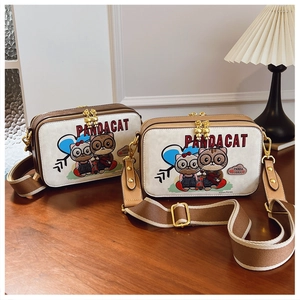 Close-up of two cartoon bear print shoulder bags with golden hardware on wooden table