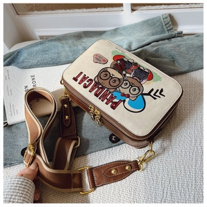 Detail view of the retro cartoon cat print and gold hardware on the cream shoulder bag