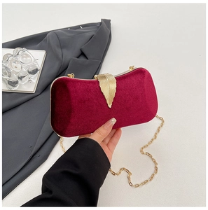 Detail of burgundy velvet clutch featuring a gold leaf clasp and fine chain strap