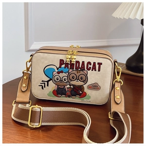Detail view of cartoon cat embroidery and gold hardware on beige shoulder bag